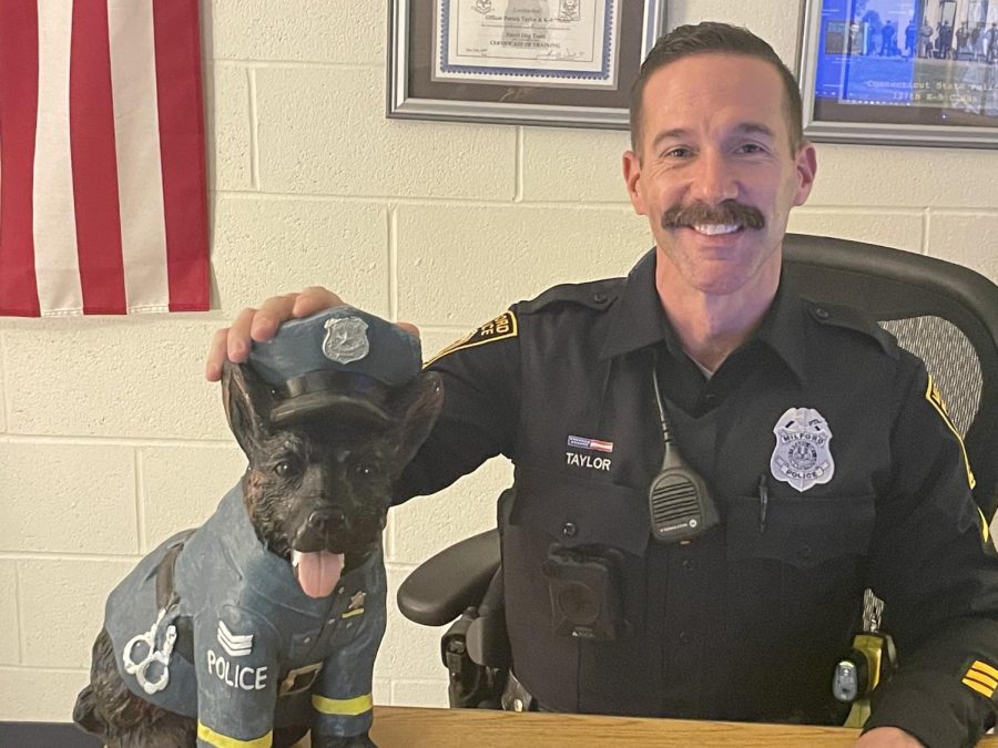 Photograph of Officer Taylor sitting at his desk with his fake dog.